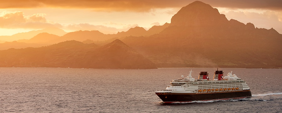 A Disney cruise ship sails past a mountainous shore