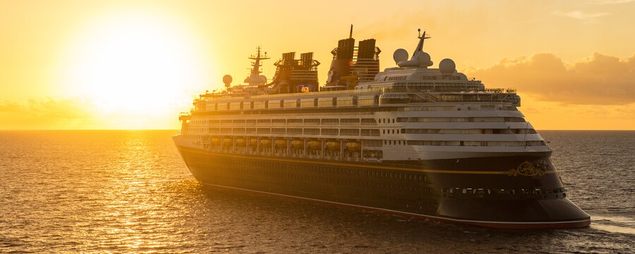 A Disney Cruise ship sails on the ocean, towards the sun setting on the horizon